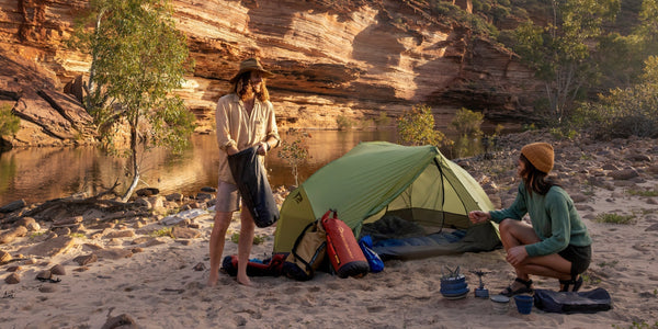 Two people camping by a river with a Sea to Summit tent and gear set up on the sand.