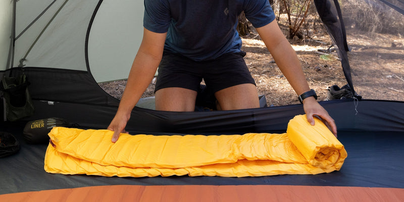 Person rolling up a yellow sleeping bag inside a tent.