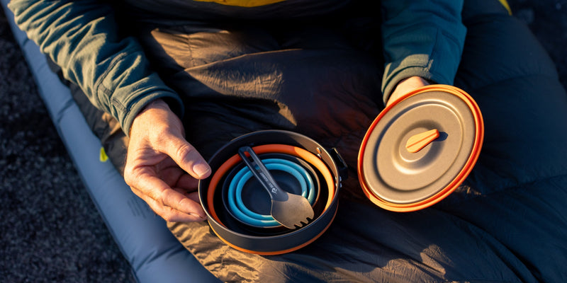 Person sitting outdoors holding a camping cookware set