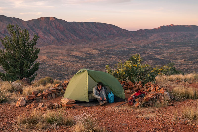 a woman sits in nature in her tent and ties her hiking boot 