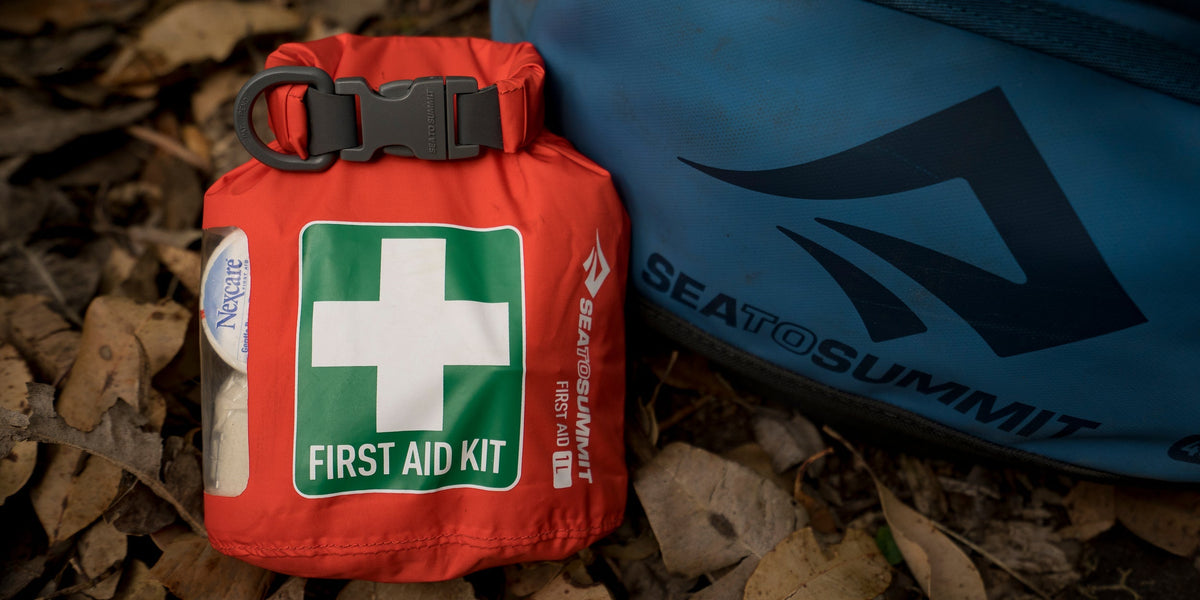 Close-up of a red first aid kit on the ground next to a blue Sea to Summit bag.
