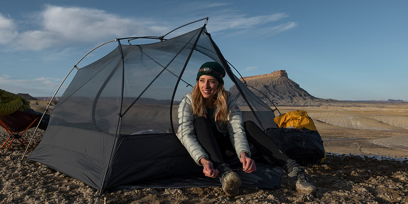 woman sits in an inner tent in nature and ties her hiking boots 