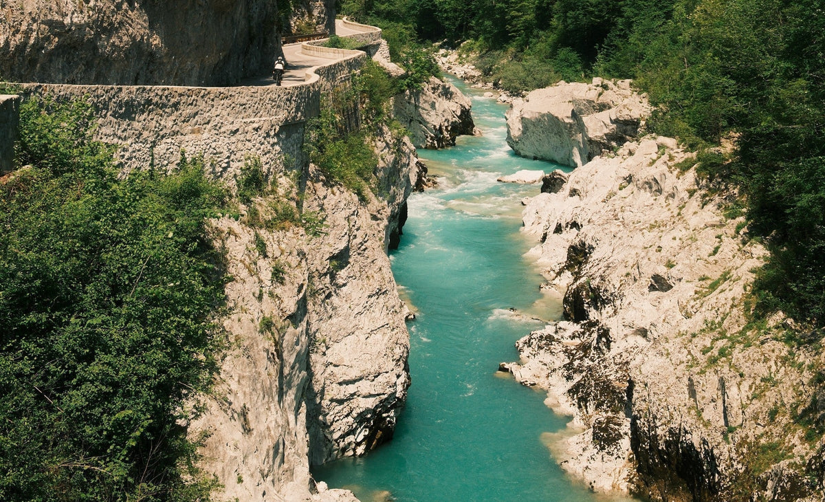 Turquoise river flowing through a narrow rocky canyon, surrounded by lush green trees and a winding path above the cliffs.
