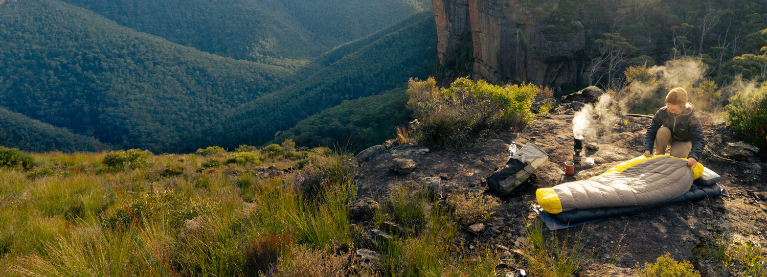 A woman next to her Spark Women's sleeping bag in the blue mountains.