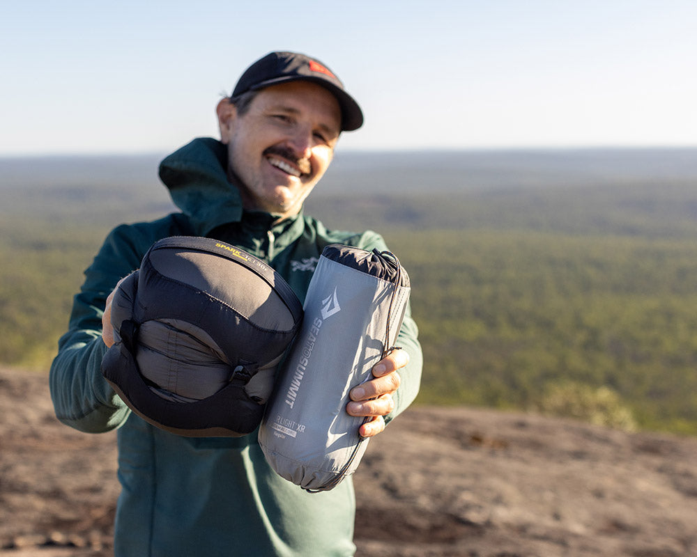 A man smiling at the camera showing some Sea to Summit products