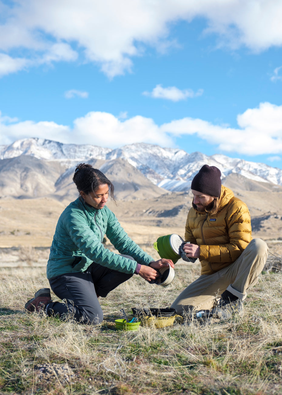 Two people in the outdoors in front of a beautiful mountain, cleaning their camp kitchen gear.